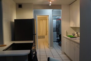 Une cuisine compacte équipée d’un réfrigérateur, d’une cuisinière et d’un évier. Une porte donne accès à une salle de bain avec un rideau de douche.