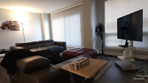 Ein Wohnzimmer mit einer Couch, einem Tisch, einem Fernseher und einem Fenster mit Jalousien.