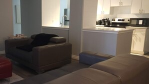 Ein Wohnzimmer mit einer Couch, einem Hocker und einem Flachbildfernseher.
