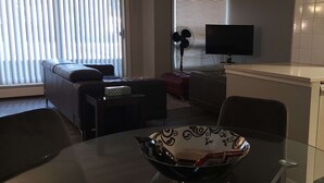 Ein modernes Wohnzimmer mit einer Couch, einem Esstisch mit einer Schüssel, einem Fernseher und einer Küchenzeile mit Spüle und Schränken.