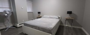 Et soveværelse med seng, sengeborde, en ventilator og et vindue med persienner.