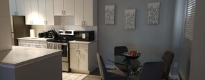 A modern kitchen with white cabinets, a black microwave, and a glass dining table with two chairs. - Corporate Apartment in Downtown Calgary (Calgary)