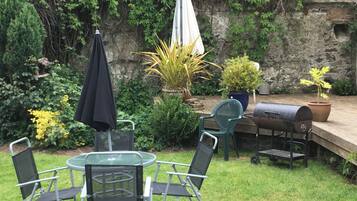 A patio with a round table and chairs, a grill, and potted plants.