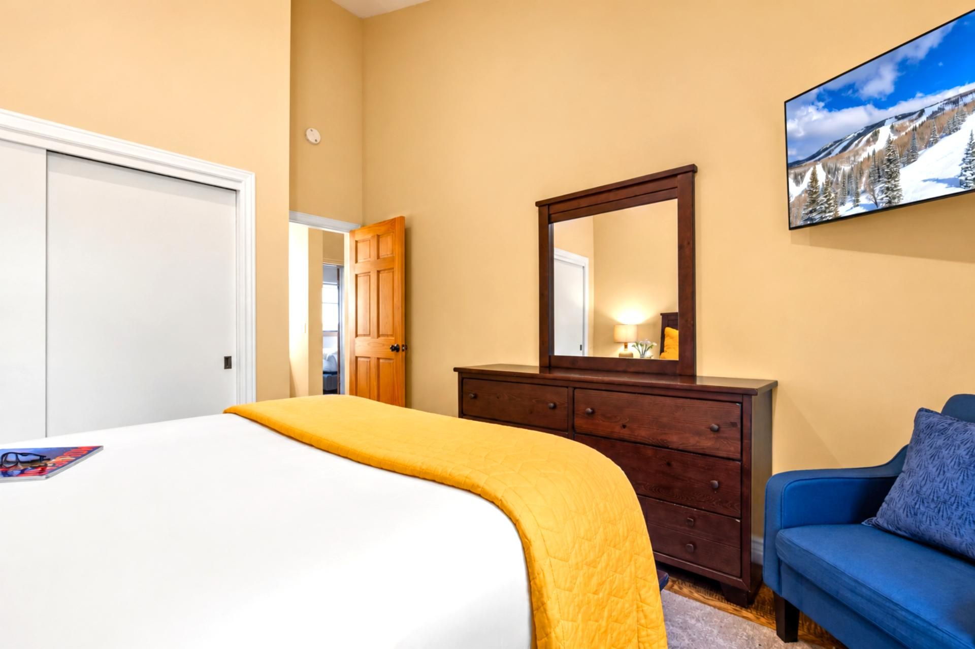 Una habitación de hotel con una cama, un aparador, un espejo, un sofá azul y un cuadro en la pared.
