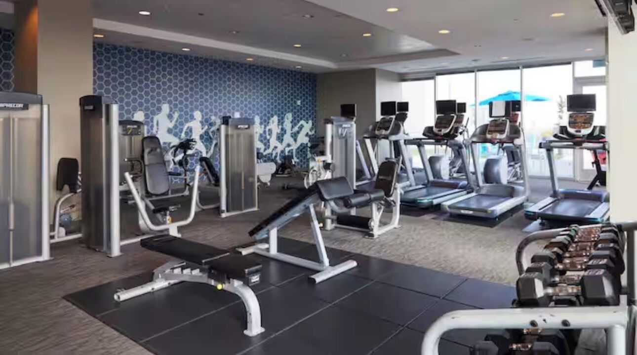 A gym with cardio machines, weight benches, and dumbbells.