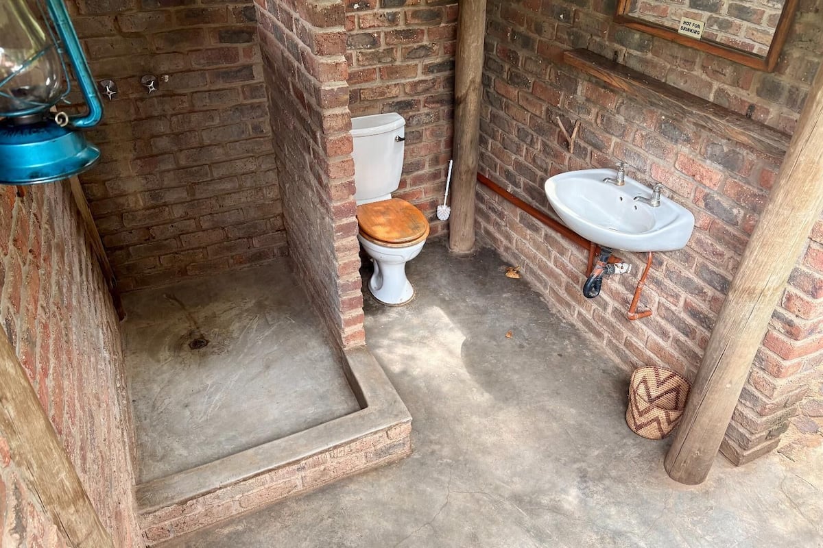A small, rustic bathroom with a wooden toilet, a white sink, and a blue lantern.