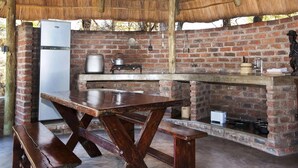 Una cocina rústica al aire libre con pared de ladrillo, mesa de madera y techo de paja.
