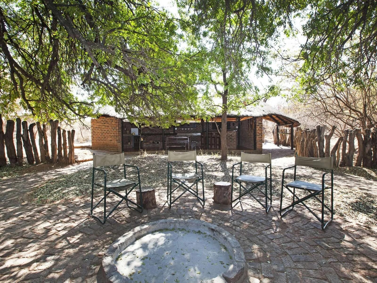 An outdoor seating area with chairs and a fire pit, surrounded by trees and a brick building.