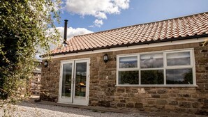 A stone building with a tiled roof, a large window, and a door.