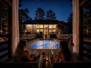Ein Poolbereich mit zwei sitzenden Personen, einem Pool und einem Gebäude mit großen Fenstern im Hintergrund.