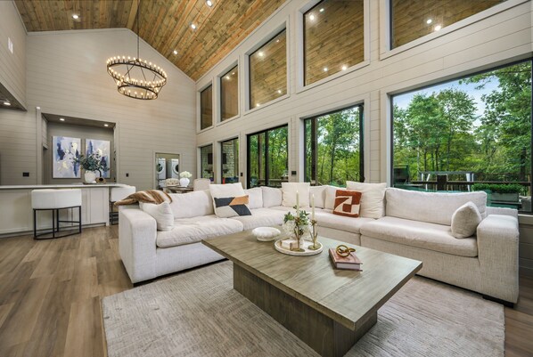 A spacious living area with a large sofa, a coffee table, and a kitchen area with a washing machine. - Creekfront Estate | Sleeps 21 | Pool & Court (Broken bow)