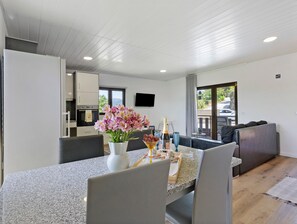 Et moderne køkken med hvide skabe, et spiseområde med et granitbord og en opholdsstue med sofa og fjernsyn ophængt på væggen.