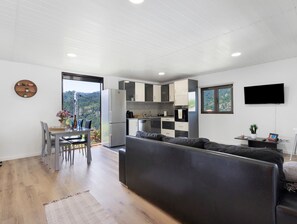 Una cocina moderna con horno y refrigerador integrados, un comedor con mesa y sillas, un sofá y un televisor montado en la pared.