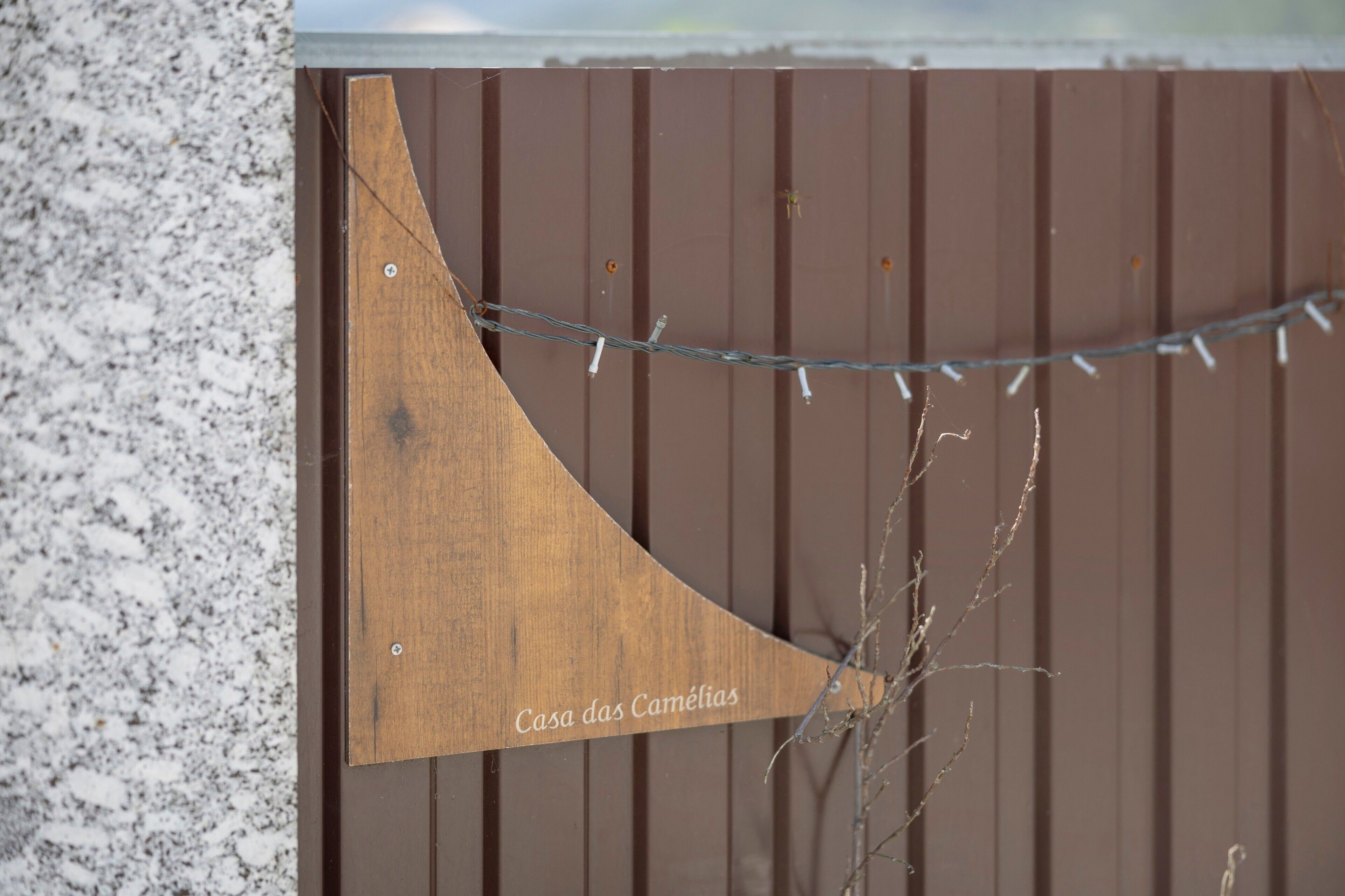 Et træskilt med teksten 'Casa das Camélias' monteret på et hegn.