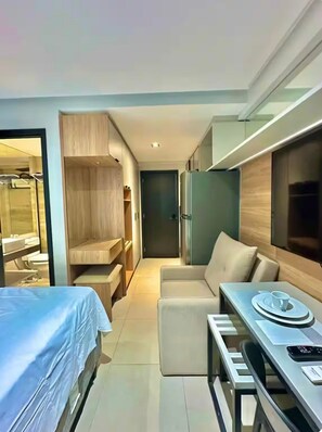 Ein modernes Hotelzimmer mit Bett, Sofa, Esstisch, integriertem Fernseher und separatem Badezimmerbereich.