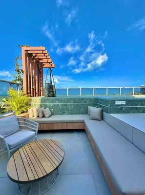 Eine Dachterrasse mit einer Holzpergola, einer Sitzecke und Blick auf den Ozean.