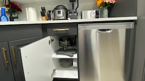 Une cuisine compacte avec des meubles gris, une machine à café, un four à micro-ondes, un mixeur et un lave-vaisselle.
