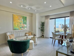 Ein modernes Wohnzimmer mit einer Couch, einem grünen Sessel, einem Esstisch und einem großen Fenster mit Blick auf die Stadt.