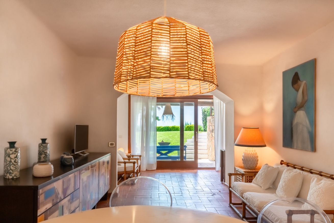 Een moderne woonkamer met een grote geweven lamp, een witte bank, een eettafel en een televisie op een donkere kast.