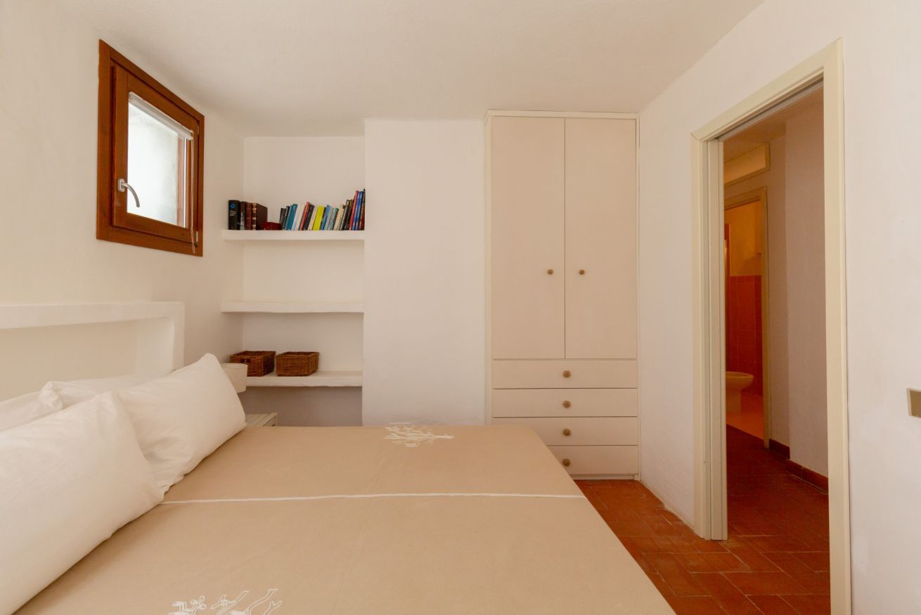 A bedroom with a bed, a wardrobe, a shelf with books, and a mirror.