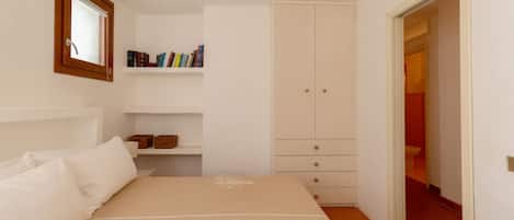 A bedroom with a bed, a wardrobe, a shelf with books, and a mirror.