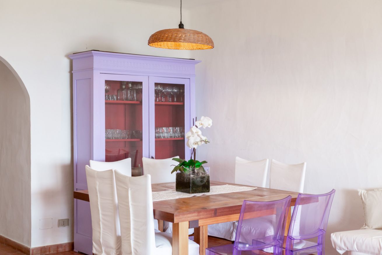 A dining area with a wooden table, white chairs, a purple cabinet with glass doors, and a hanging light fixture.