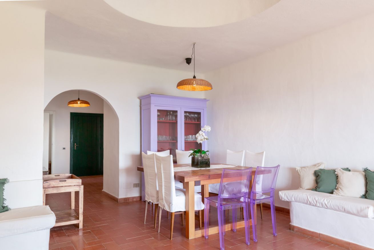 A dining area with a wooden table, white chairs, a purple cabinet, and a green door in the background.