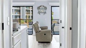 Sala moderna com sofá bege, relógio decorativo na parede e vista para uma varanda com guarda-corpo.