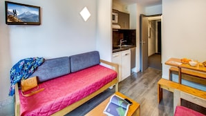 Un espacio habitable compacto con sofá, mesa de comedor, zona de cocina y un cuadro en la pared.
