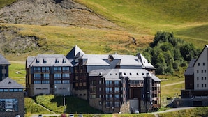 Un edificio grande de varios pisos con un diseño arquitectónico moderno, ubicado en una colina con vistas del paisaje circundante.