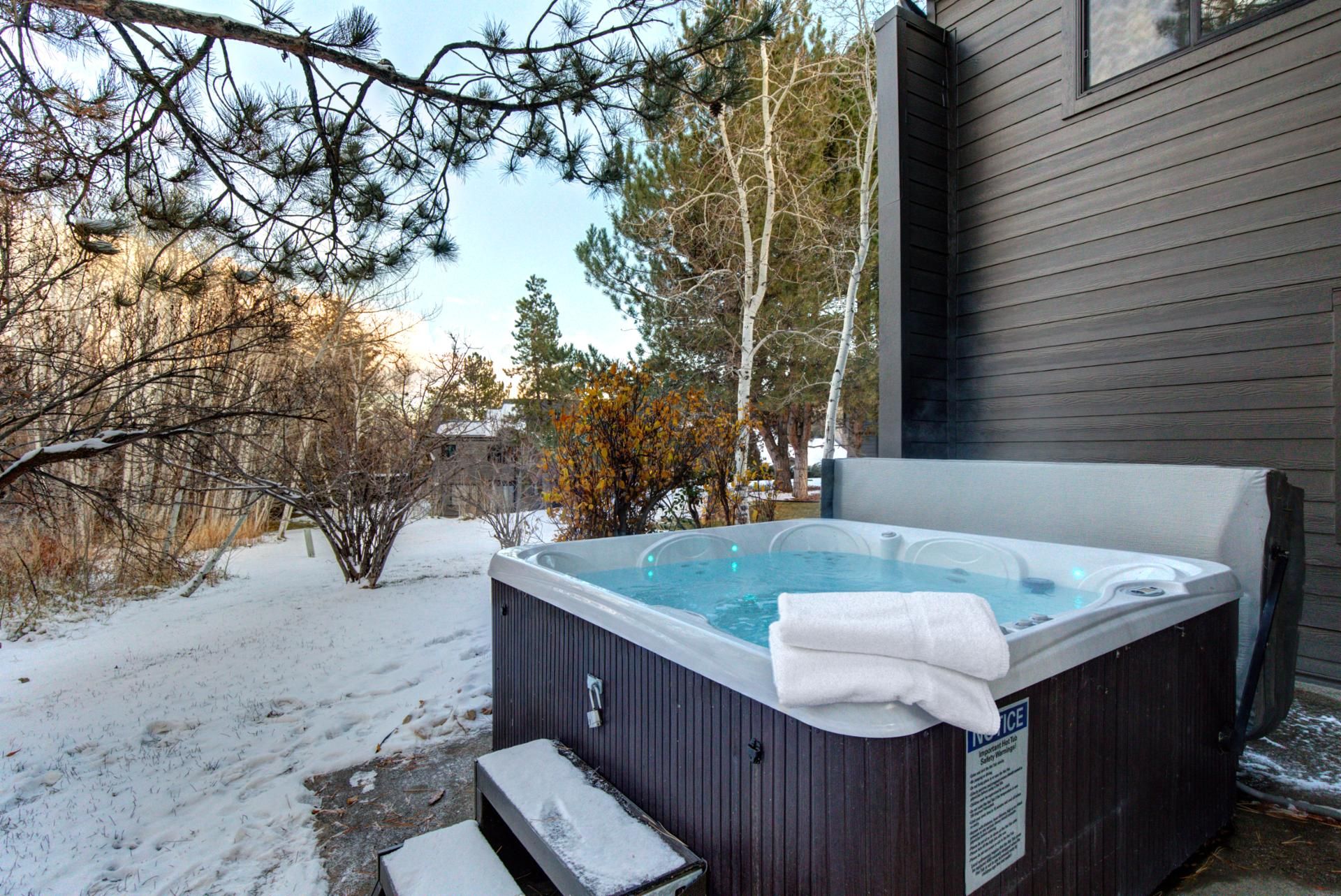 A hot tub outside a house with a wooden deck and snow on the ground.