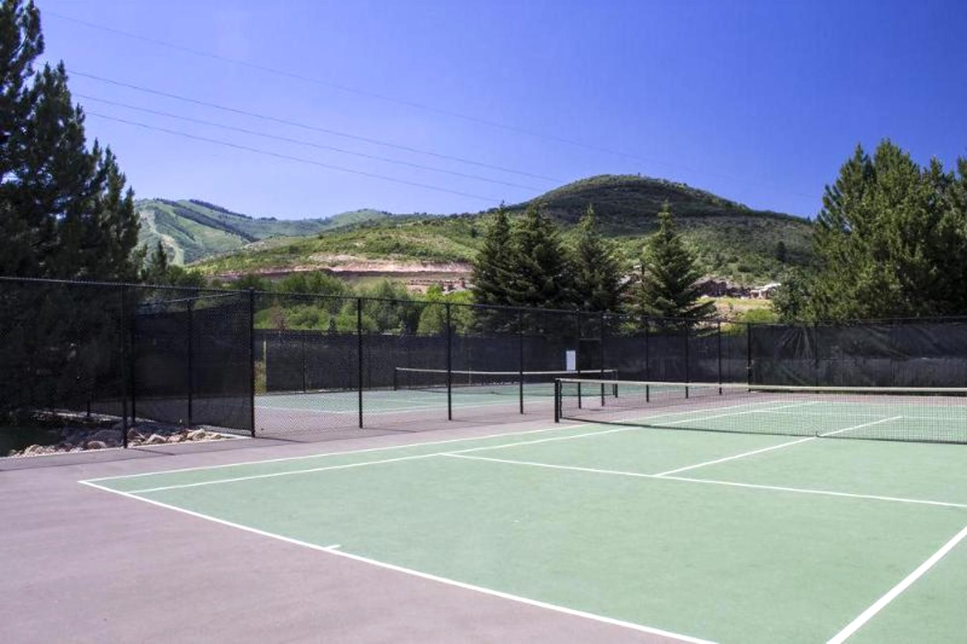 Ein Tennisplatz im Freien mit Netz, umgeben von einem Zaun und Bäumen.