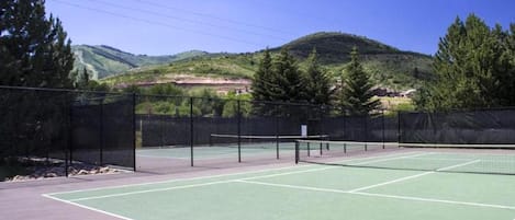 Ein Tennisplatz im Freien mit Netz, umgeben von einem Zaun und Bäumen.
