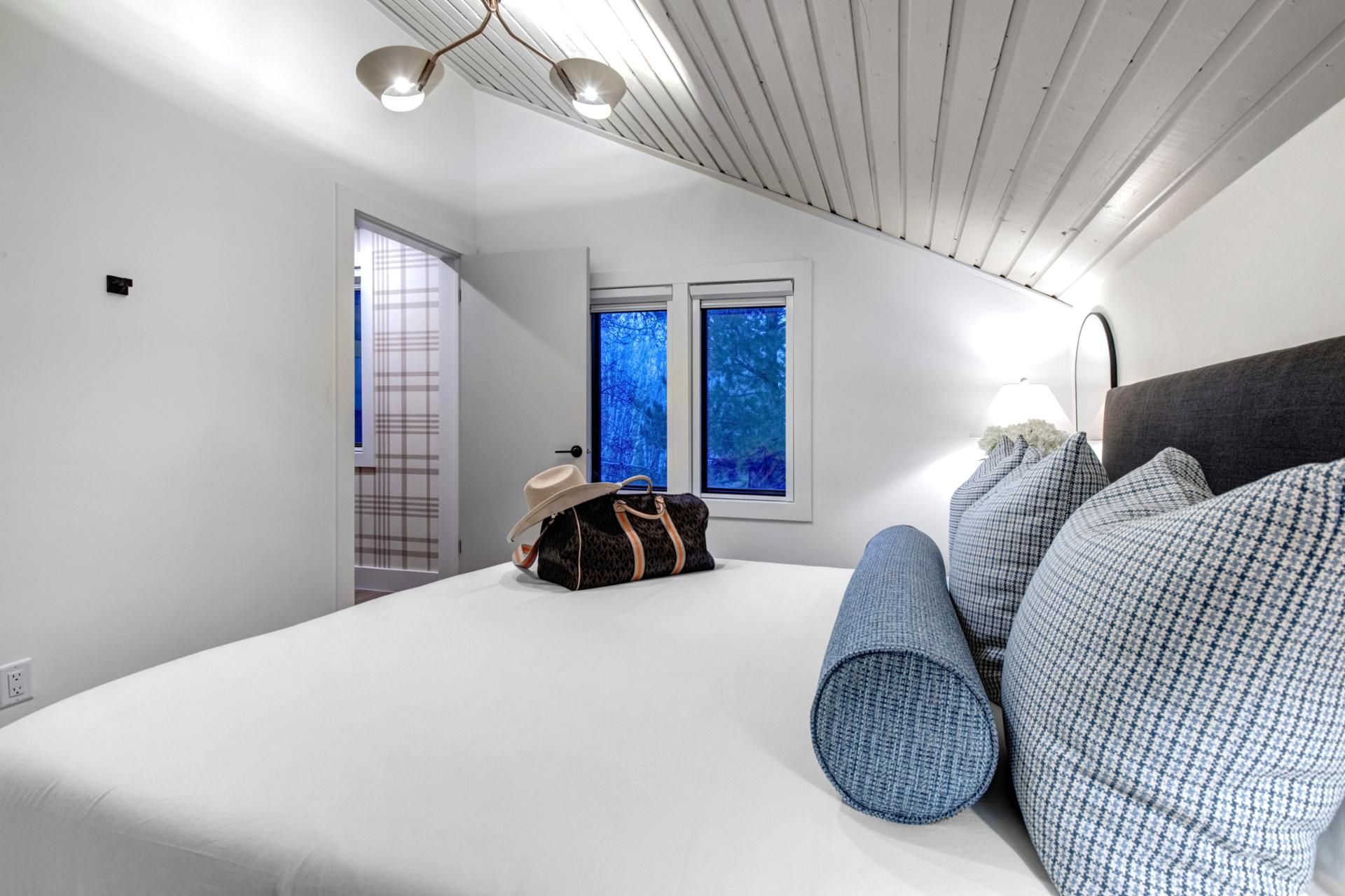 Une chambre avec un grand lit, une valise et une fenêtre donnant sur des arbres.