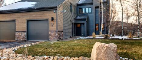 A modern two-story house with a stone foundation, a garage, and a large rock in the front yard.