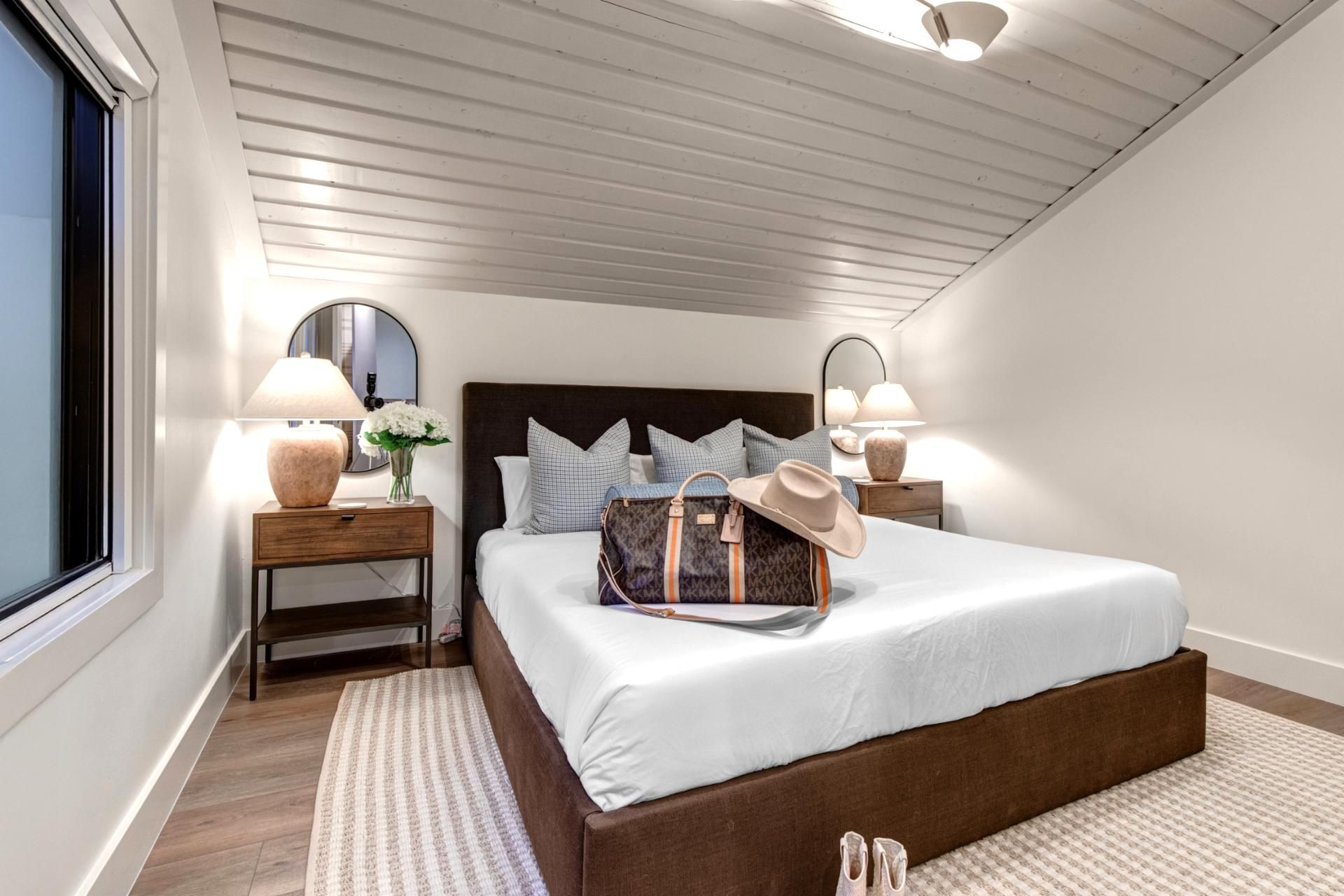 Un dormitorio con una cama grande, dos mesitas de noche, un espejo y una ventana.