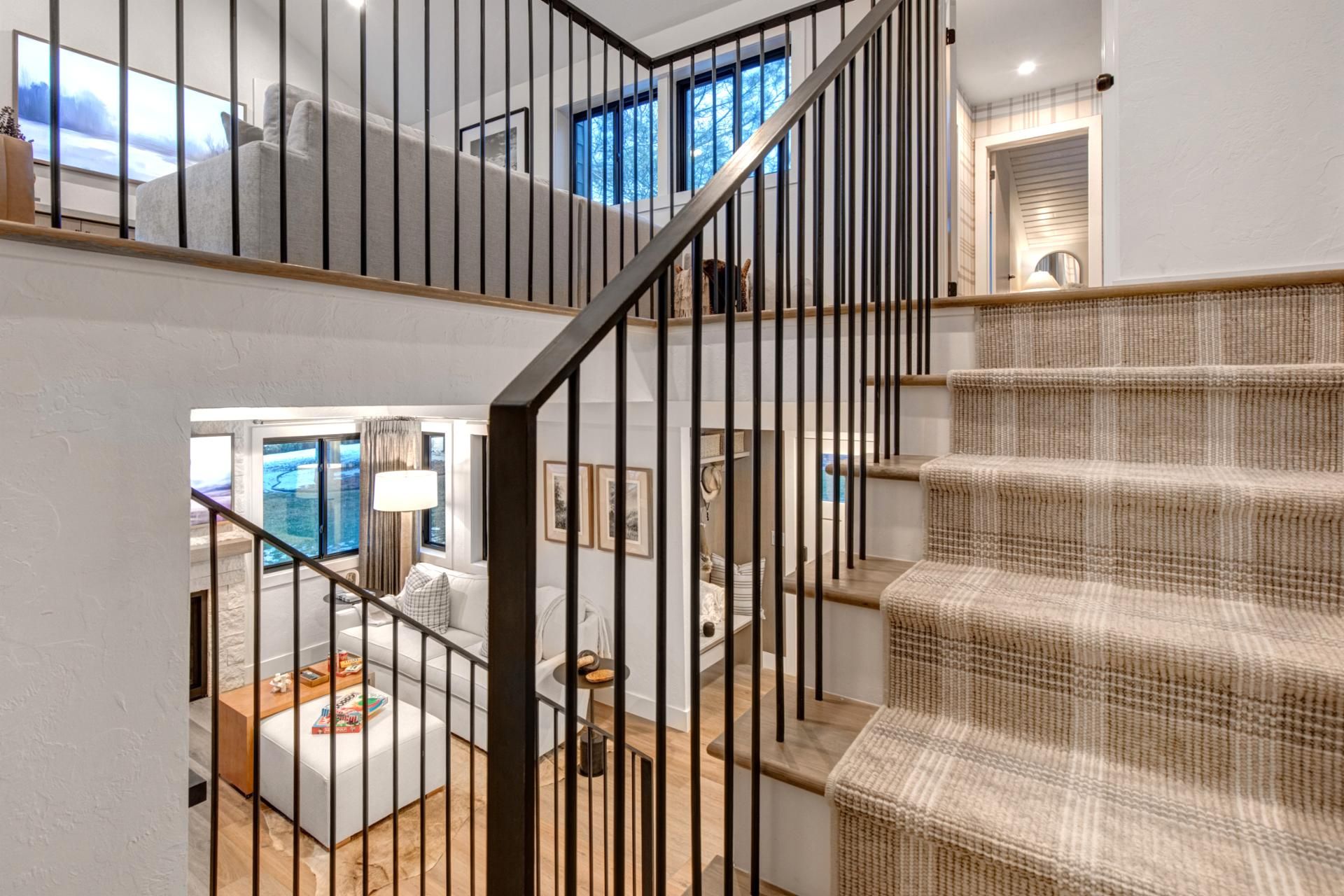 Eine Treppe mit gewebtem Teppich und schwarzen Metallgeländern, die zu einem Zimmer mit Ausblick auf die Außenwelt führt.