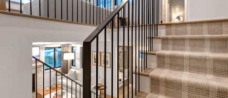 Un escalier recouvert d’une moquette à motifs et doté de rampes en métal noir, menant à une pièce offrant une vue sur l’extérieur.