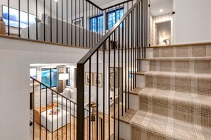 Una escalera con un tapete tejido y barandillas de metal negro, que conduce a una habitación con vistas al exterior.