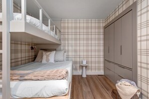 Ein Schlafzimmer mit Etagenbett, Nachttisch, Kleiderschrank und raumhoher Tapete mit Karomuster.