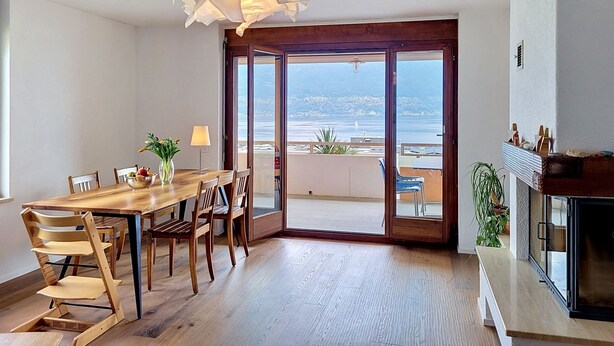 A dining area with a wooden table and chairs, a vase with flowers, and a view through a glass door to the outside. - Casa Rivapiana by Interhome (Muralto)