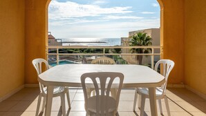 A balcony with a table and chairs, a pool, and a view of the sea and buildings. - Sea View Apartment for 4 in Valras-plage (Valras-Plage)