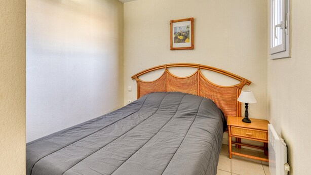 A bedroom with a bed, a nightstand, a lamp, a picture on the wall, and a window with blinds. - Sea View Apartment for 4 in Valras-plage (Valras-Plage)