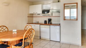 A compact kitchen with a microwave, coffee maker, and dishwasher, a dining table with chairs, and a window with a view. - Sea View Apartment for 4 in Valras-plage (Valras-Plage)