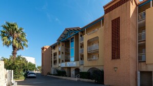 A multi-story hotel with balconies, a parking lot, and a palm tree. - Sea View Apartment for 4 in Valras-plage (Valras-Plage)