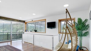 A spacious room with a large window, a hanging chair, a flat-screen TV, and a potted plant. - Apartment 'Casa Do Lagar' with Lake View, Wi-Fi and Air Conditioning (Geres)