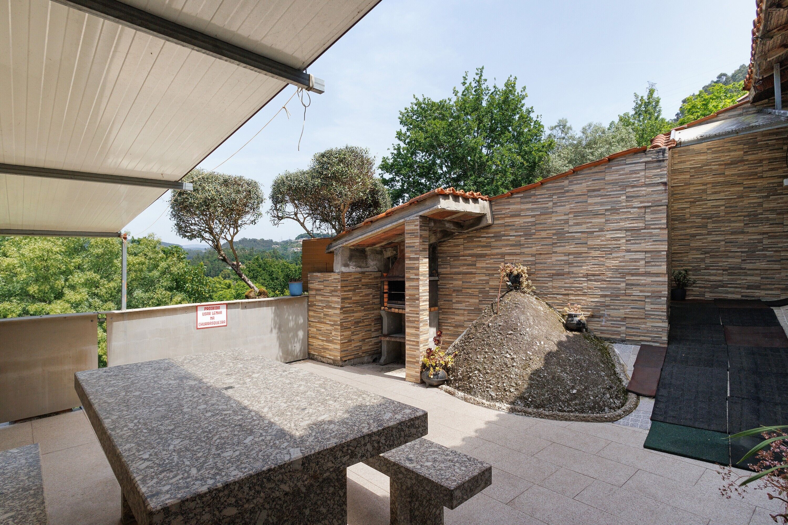 A covered outdoor area with a stone wall, a table, and a barbecue grill.