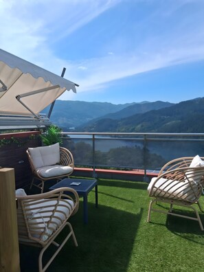 A terrace with wicker furniture, a table, and a view of a lake and mountains. - Apartment 'Casa Do Lagar' with Lake View, Wi-Fi and Air Conditioning (Geres)