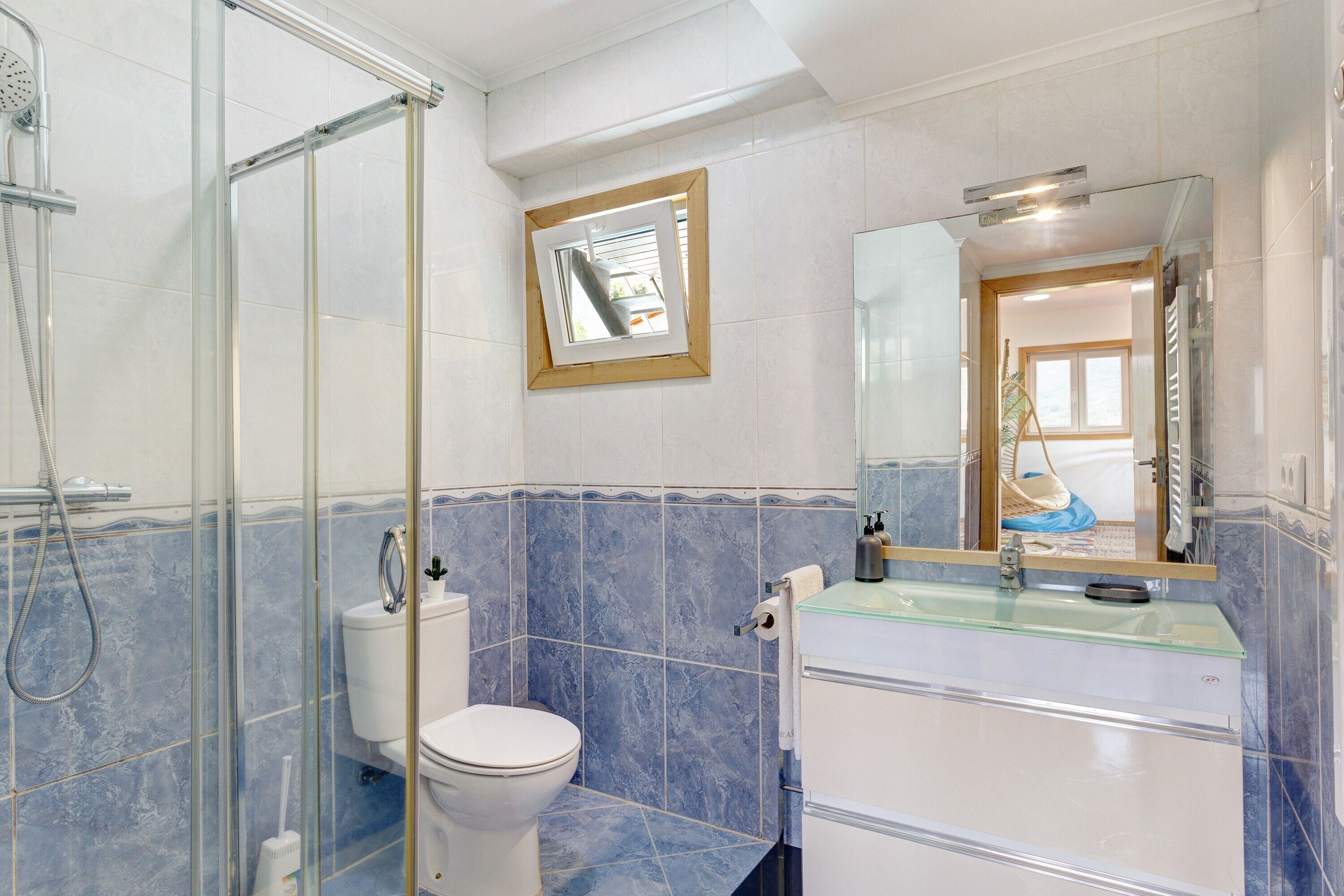 Une salle de bain avec une douche à parois de verre, des toilettes, un lavabo avec un miroir et un tableau encadré au mur.