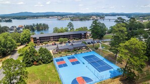 Vista aérea de un complejo deportivo con cancha de tenis, un edificio y un río al fondo.